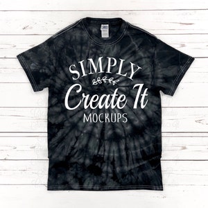 May include: A short-sleeve crew neck t-shirt featuring a black and grey spiral tie-dye pattern. The front displays white text that reads SIMPLY Create It MOCKUPS with a small decorative leaf graphic centred between the first two lines of text.