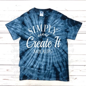 May include: A short-sleeved crew neck t-shirt featuring a dark blue and white spiral tie-dye pattern. The front displays white text that reads SIMPLY Create It MOCKUPS with a small decorative leaf graphic centred between the first two lines.