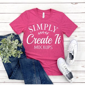 Pode incluir: Uma camiseta magenta com o texto branco "SIMPLY Create It MOCKUPS", combinada com jeans azuis e tênis brancos. Um ramo de vegetação é colocado perto dos jeans. Os itens estão dispostos sobre madeira.