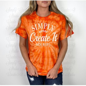 May include: A tie-dye orange t-shirt with the text "SIMPLY Create It MOCKUPS" in white. The shirt is a short-sleeved crew neck style.