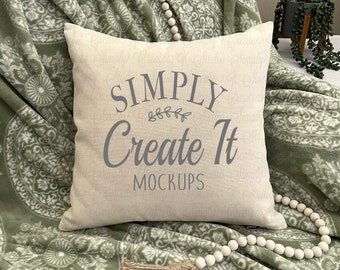 May include: A white throw pillow with the text "SIMPLY Create It MOCKUPS" on a green and white patterned throw blanket with a wooden bead garland.