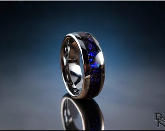 May include: A polished silver ring with a dark blue and purple inlay. The ring is set against a dark blue background, with a reflection visible below. The inlay has a speckled appearance.