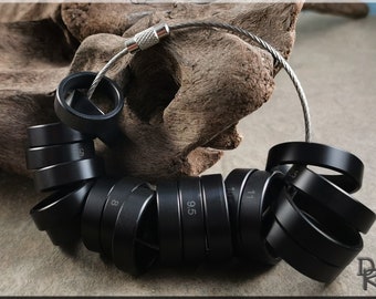 May include: A set of black metal ring sizers, numbered 5 through 13, connected by a silver chain. The sizers are arranged in a circle, with the numbers facing outward.