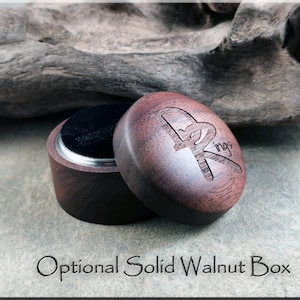 K&ouml;nnte beinhalten: Ge&ouml;ffnete Ringbox aus massivem Walnussholz mit schwarzem Samtinnenraum. Der Deckel ist mit einem Logo graviert und der Text "Optional Solid Walnut Box" befindet sich unter der Box. Die Box steht auf einer grauen Oberfl&auml;che.