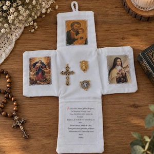Może przedstawiać: Biały, krzyżowy zestaw dewocjonalny z tkaniny z nadrukowanymi ikonami religijnymi przedstawiającymi świętego Józefa z Dzieciątkiem Jezus, Maryję Pannę i świętą Teresę. Zawiera złoty metalowy krzyżyk, dwa małe medaliki oraz tekst w języku francuskim.