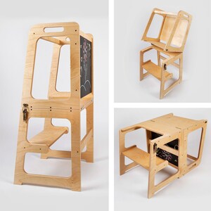 May include: A wooden learning tower with a chalkboard panel and a step. The tower is made of light-colored wood and has a handle at the top. The chalkboard has a drawing of a flower. The tower can be folded into a table.