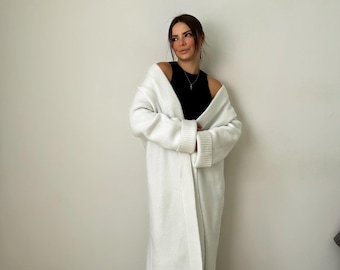 Op de afbeelding: Een lange witte cardigan met een shawlkraag en lange mouwen. De cardigan is open aan de voorkant en heeft een geribbelde zoom en manchetten.