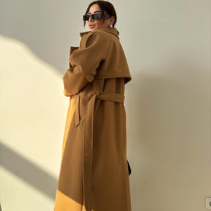 May include: A long, camel-colored coat with a belt and a wide collar. The coat is made of a soft, warm fabric and has a classic, elegant style.