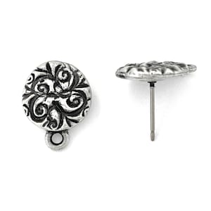 May include: Two silver-toned stud earrings. Each earring features a round, ornate design with swirling patterns. One earring is shown from the front, the other from the side, revealing the post and backing. The earrings are set against a white background.