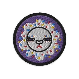 May include: A purple and white embroidered patch with a donut design. The donut has a white frosting with colorful sprinkles and a cartoon face with closed eyes and a frown.