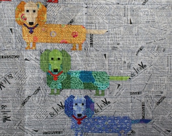 Könnte beinhalten: Eine Patchwork-Decke mit fünf Dackeln in verschiedenen Farben und Mustern. Die Hunde sind vertikal angeordnet, wobei der oberste Hund rot ist, gefolgt von gelb, grün, blau und lila. Der Hintergrund der Decke ist ein weißer Stoff mit Zeitungsdruck.