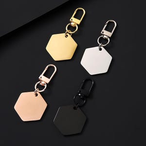 Puede incluir: Cuatro llaveros metálicos con colgantes hexagonales. Los llaveros son de color dorado, plateado, oro rosa y negro. Cada llavero tiene un cierre de mosquetón para sujetar fácilmente a llaves o bolsos. Los colgantes son lisos y brillantes.