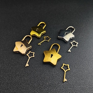 May include: A collection of star-shaped padlocks and keys in gold, silver, and bronze tones. The padlocks have a classic design with a keyhole, and the keys are shaped like stars. The items are arranged on a dark surface.