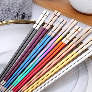 May include: A set of 12 pairs of chopsticks with colorful accents. The chopsticks are made of stainless steel and have a sleek, modern design.