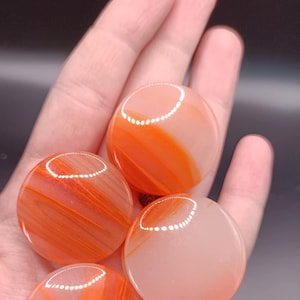 Peut inclure: Quatre pierres d'agate rondes, lisses, orange et blanches avec une finition polie. Les pierres ont un motif tourbillonnant d'orange et de blanc.