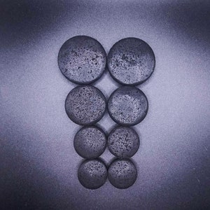 Peut inclure: Un ensemble de huit pierres rondes noires disposées en forme de pyramide. Les pierres sont lisses et ont une surface légèrement texturée.