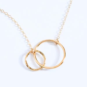 May include: A gold necklace with two interlocking circles. The smaller circle has a textured surface.