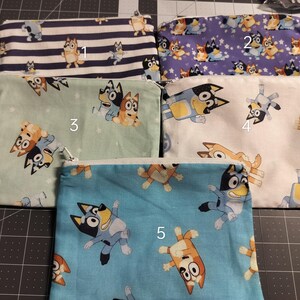 May include: Five rectangular fabric zipper pouches featuring cartoon dog characters. Pouch 1 has navy stripes, 2 is purple with stars, 3 is light green, 4 is cream, and 5 is bright blue. Each pouch is numbered 1 through 5 and displays various poses of the characters.