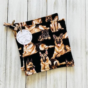 May include: Two black pot holders with a repeating pattern of German Shepherds in various poses. The pot holders have a loop for hanging and a tag that reads "Mountain Girl Creations."