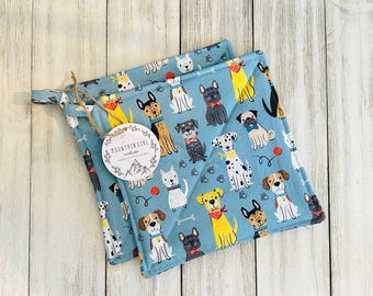 May include: Two blue quilted pot holders with a pattern of colorful dogs on a white background. The pot holders have a loop for hanging. The tag says "Mountain Girl Creations".