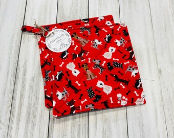 May include: Two red quilted pot holders with a repeating pattern of various dog breeds and bones. The pot holders have a loop for hanging and a tag that reads "Mountain Girl Creations."