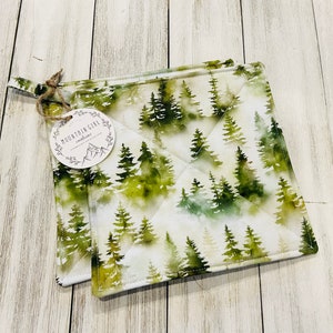 May include: Two green and white quilted pot holders with a watercolor forest print. The pot holders have a tag that says "Mountain Girl Creations".