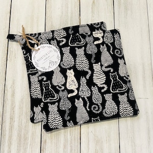 May include: Two black and white cat-patterned pot holders with a white tag that says "Mountain Girl Creations".