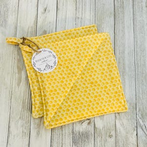May include: Two yellow quilted pot holders with a honeycomb pattern. The pot holders have a loop for hanging and a tag that says "Mountain Girl Creations".