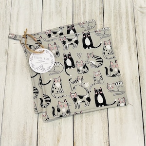 May include: Two gray cotton pot holders with a black and white cat pattern. The pot holders have a pink heart and the text "Mountain Girl Creations" on one of the pot holders.