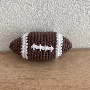 May include: A brown and white crocheted football. The football has white stitching.