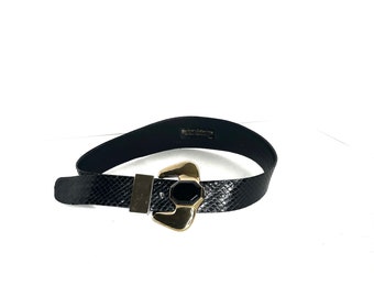May include: Black leather belt with a gold and black buckle. The buckle is shaped like a geometric design with a black stone in the center. The belt is embossed with a snake skin pattern. The belt is labeled "Barneys Collection" on the back.