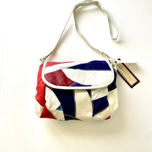 Könnte beinhalten: Eine weiße Leder-Patchwork-Umhängetasche mit roten, blauen und weißen Lederstücken. Die Tasche hat einen weißen Riemen und ein kleines Etikett mit der Aufschrift "Dina & Lily".
