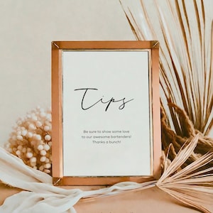 May include: A copper-framed sign with the word "Tips" in a handwritten font. The sign reads "Be sure to show some love to our awesome bartenders! Thanks a bunch!"