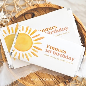 May include: White chocolate bar wrapped in foil with a sun design and the text "Emma's 1st birthday" in orange and pink. The text "Thank you for celebrate with us" is also included in smaller font.