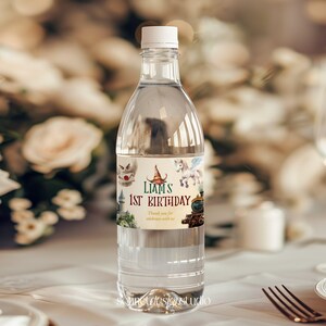 May include: Clear plastic water bottle with a white cap and a custom label. The label reads "Liam's 1st Birthday" with illustrations of a train, a unicorn, and other whimsical images. The bottle is filled with clear liquid.