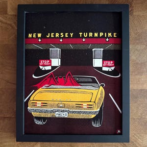 May include: A framed art print featuring a yellow convertible car with a red bat figure in the back seat, driving toward New Jersey Turnpike toll booths. The text reads NEW JERSEY TURNPIKE and STOP GET TICKET. The license plate says PINEZ 13.