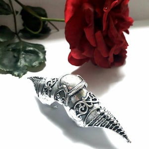 Könnte beinhalten: Ein silberner Krallenring mit filigranen Details. Der Ring ist für den Mittelfinger konzipiert und hat eine spitze Krallenform.