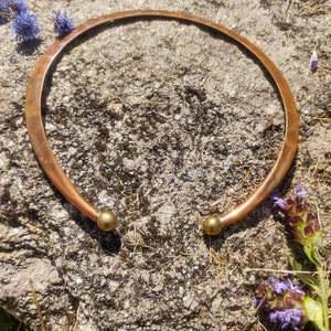 Könnte beinhalten: Eine Kupferkette mit zwei goldfarbenen Kugelakzenten. Die Kette liegt auf einer rauen, grauen Steinoberfläche.