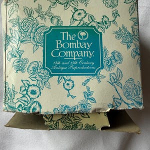 May include: A vintage box from The Bombay Company, with a cream background and a teal floral pattern. The box has a teal label with the company name and the text "18th and 19th Century Antique Reproductions."