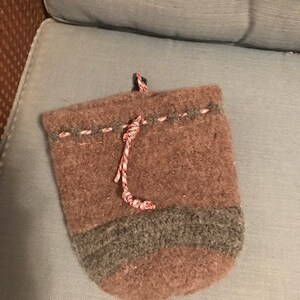 Puede incluir: Una bolsa de cordón de punto marrón con una banda de rayas grises y marrones alrededor de la parte superior. La bolsa tiene un cordón de cordón rojo y blanco.