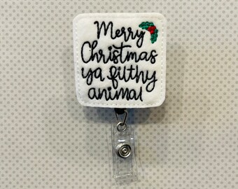 May include: White badge holder with a white square patch that says "Merry Christmas ya filthy animal" with a red and green holly design. The badge holder has a clear plastic retractable clip.