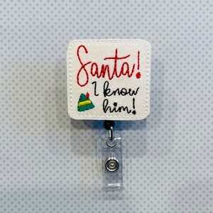 Könnte beinhalten: Weißer quadratischer Badgehalter mit einem roten gestickten Design, auf dem "Santa! I know him!" mit einem grünen Elfenhut-Motiv steht. Der Badgehalter ist an einer durchsichtigen, einziehbaren Badge-Spule befestigt.