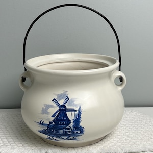 Puede incluir: Maceta de cerámica blanca con asa de metal negro. La maceta tiene un diseño de molino de viento azul y blanco.