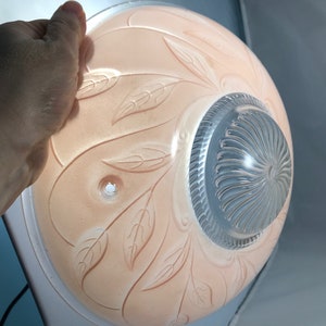 May include: A pink glass ceiling light fixture with a clear glass center and a leaf design. The fixture has two holes for mounting.