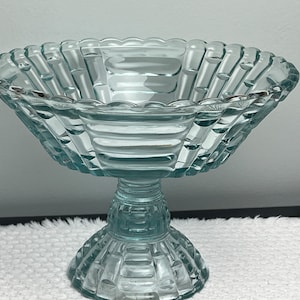 Puede incluir: Un cuenco de pedestal de vidrio transparente con un diseño acanalado. El cuenco tiene una base ancha y poco profunda y un tallo alto y delgado.