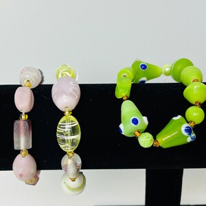May include: Three bracelets with colorful glass beads. The first bracelet has pink and white beads. The second bracelet has yellow and white beads. The third bracelet has green and blue beads.