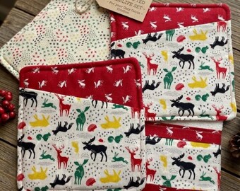 May include: A handcrafted wildlife set for the kitchen, featuring a pot holder, oven mitts, and a towel. The set has a red and white color scheme with a pattern of deer, moose, and other wildlife. The pot holder has a loop for hanging.