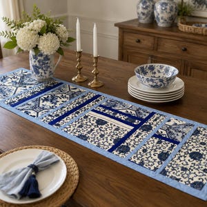 May include: A rectangular table runner featuring a patchwork design of blue and white floral patterns with solid dark blue fabric accents. The runner is constructed with a light blue border and is displayed on a wooden table with matching decor.