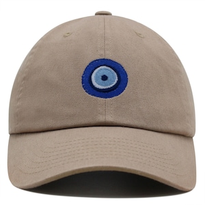 Puede incluir: Una gorra de béisbol de color caqui con un mal de ojo azul y blanco bordado en la parte delantera.