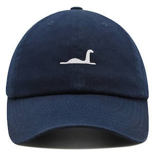 May include: A navy blue baseball cap with a white embroidered image of the Loch Ness Monster.